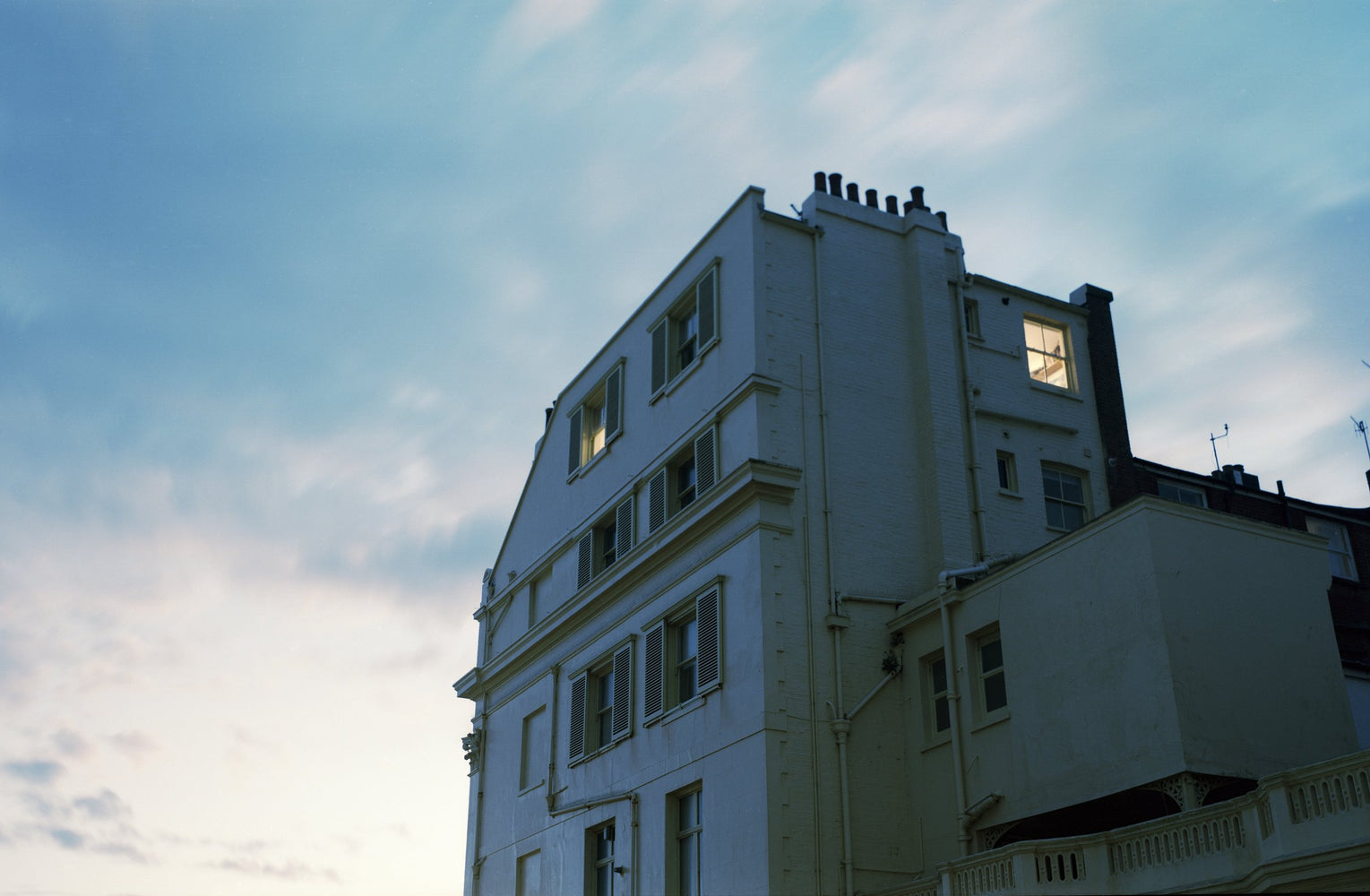 A white building with lit windows against a blue sky and clouds, shot on Kodak Portra with the Intrepid Super 120