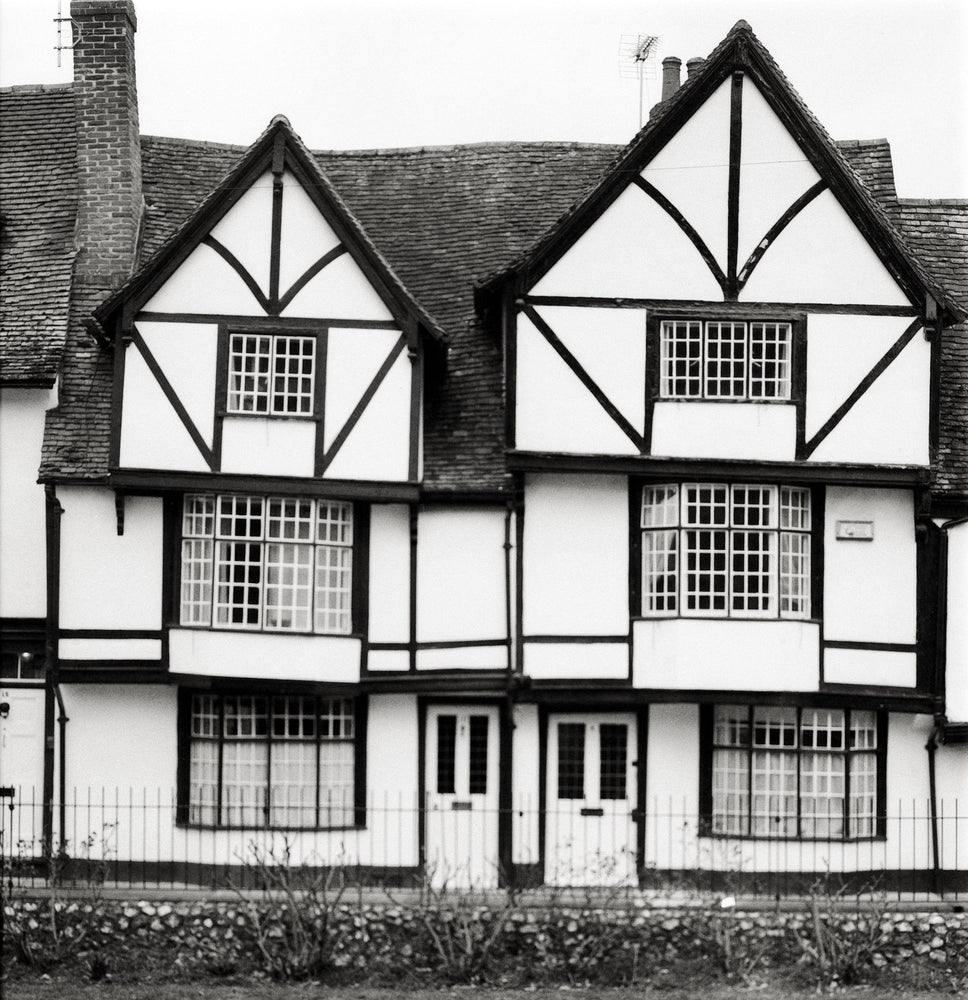 Two timber-framed Tudor houses with leaded windows behind iron railings, black and white photograph shot on the Intrepid Super 120